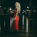 Woman in a red dress with a floral pattern standing on a wet street at night.