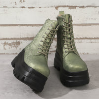 Green leather boots with black soles on a textured surface with a lantern and flowers in the background.