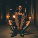 Brown knitted hoodie with fringe details on a model sitting outside with tall boots