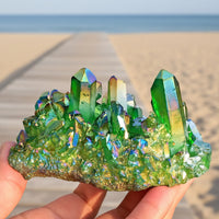A green crystal energy poly prism with multiple facets and a rough, uneven surface, held in a person's hand.