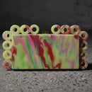 Colorful marbled soap with a decorative border held by a hand on a dark surface
