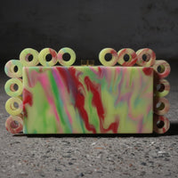 Colorful marbled soap with a decorative border held by a hand on a dark surface