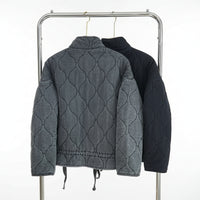 Two quilted jackets hanging on a rack against a neutral background