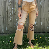 Person wearing beige ripped jeans standing in a grassy area with a wooden fence in the background.