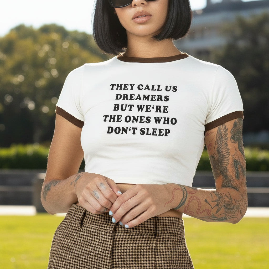 Person wearing a white crop top with text and brown pants outside on a sunny day