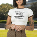 Person wearing a white crop top with text and brown pants outside on a sunny day