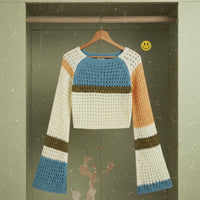 Colorful crochet sweater on a hanger against a green door with a smiley face sticker.