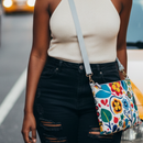 Person wearing a beige top and black ripped jeans with a colorful patterned bag, standing on a street.