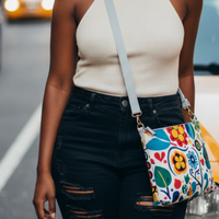 Person wearing a beige top and black ripped jeans with a colorful patterned bag, standing on a street.