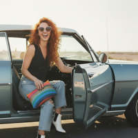 Woman with red hair sitting in an open car door, holding a colorful pillow.